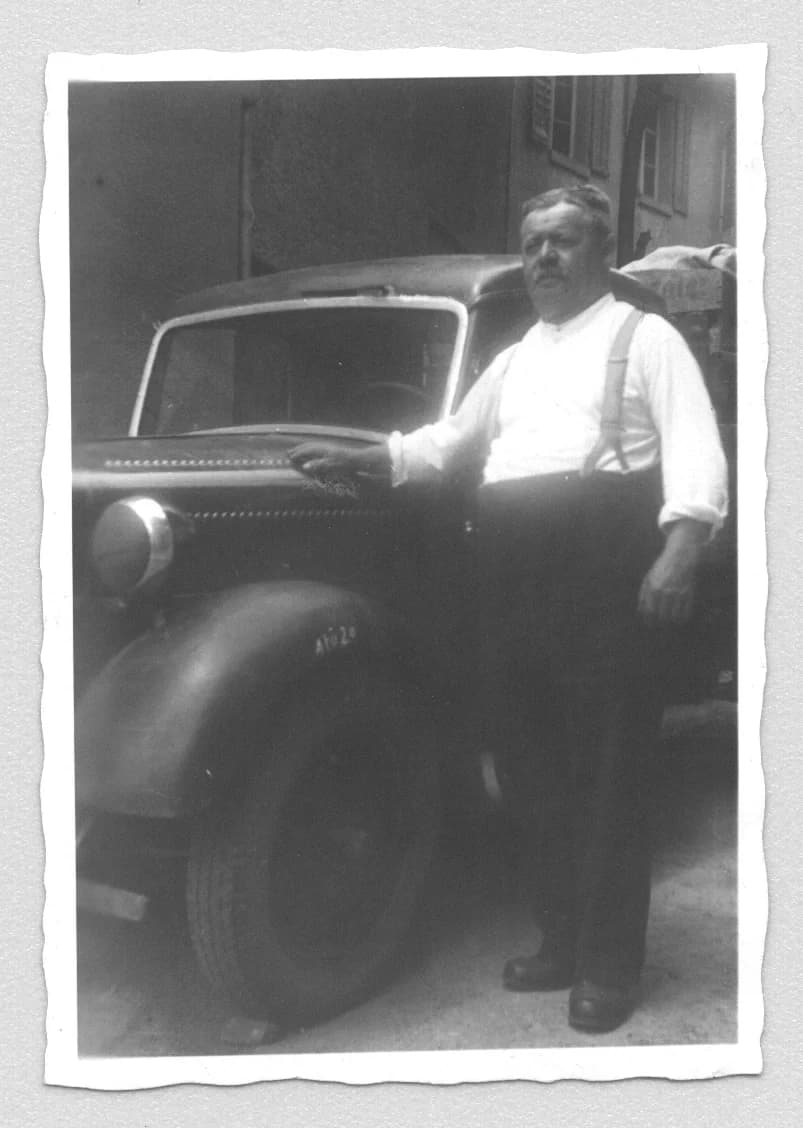 Erwin Zipse in weißem Hemd mit Hosenträgern, lehnt an einem Auto aus den 1930er-Jahren. Schwarz-Weiß-Foto.