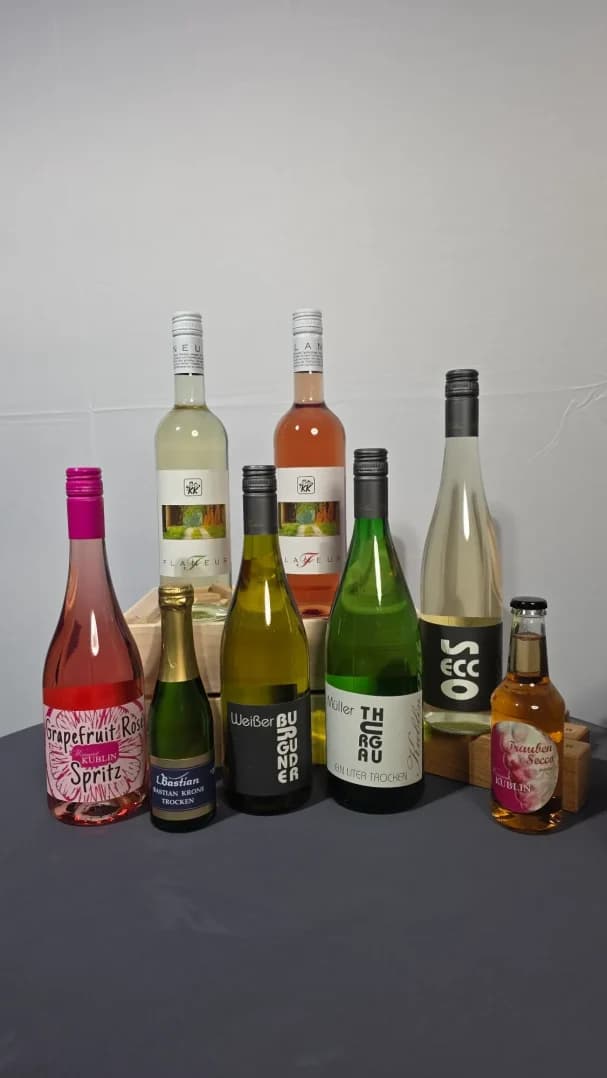 Vielfalt an Weinen und Schaumweinen in verschiedenen Flaschen auf grauem Hintergrund.
