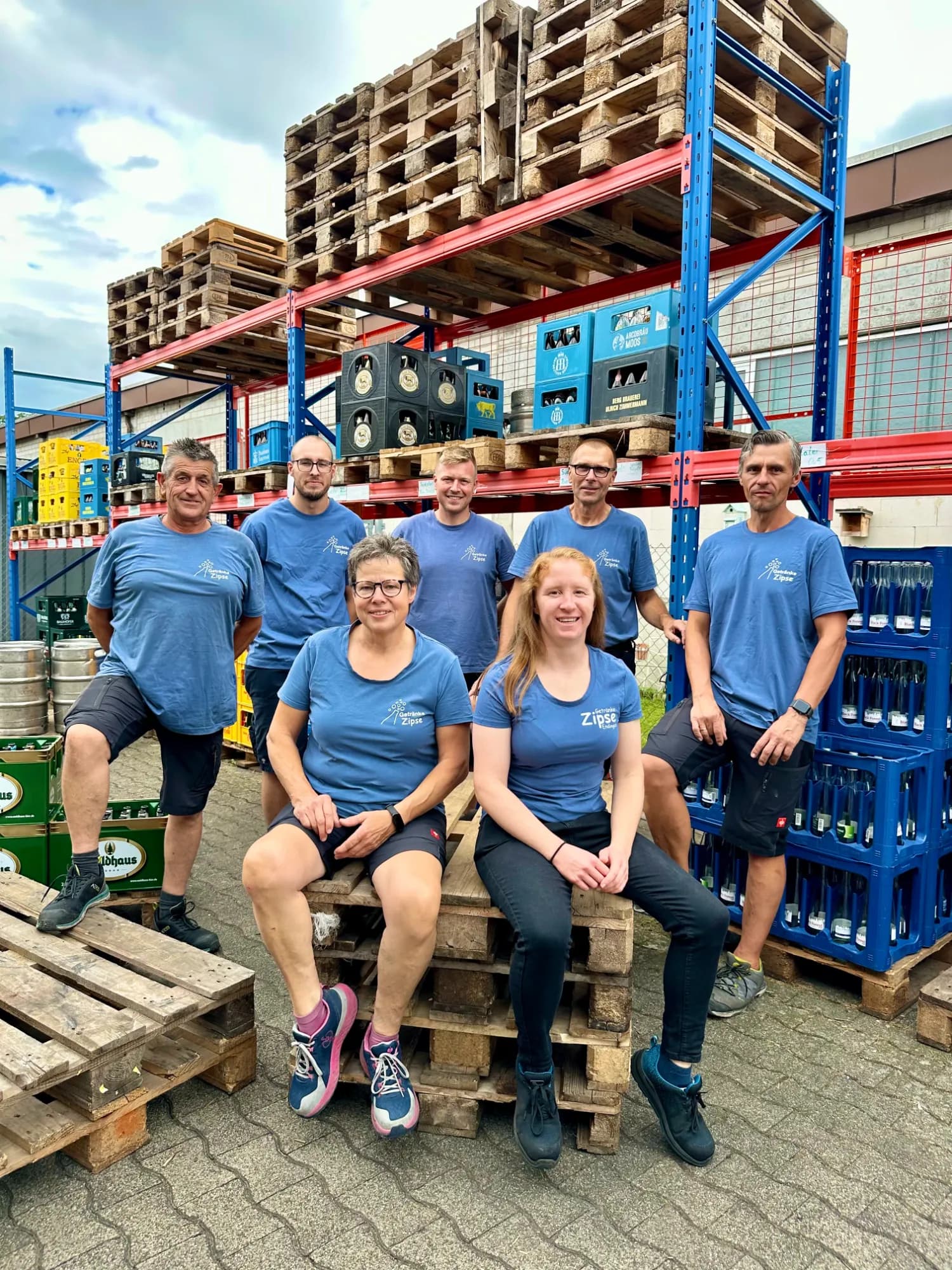 Das Team von Getränke Zipse: sechs Personen in blauen T-Shirts zwischen Getränkekästen und Paletten.